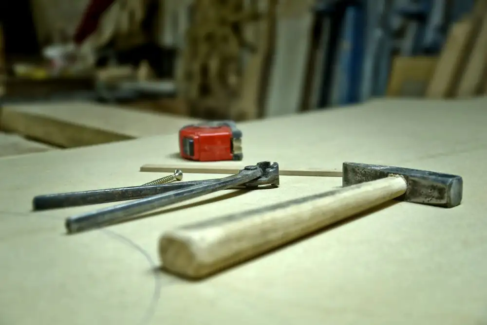 Close-up of hammer, screw, pincers, and tape measure on a workbench in a workshop.
