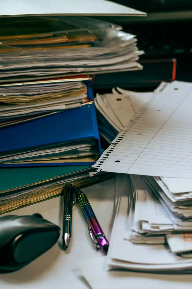 An organized desk with stacks of paper, folders, pens and a computer mouse.