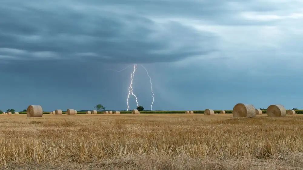 A striking image of lightning illuminating a rural hayfield under a stormy sky.