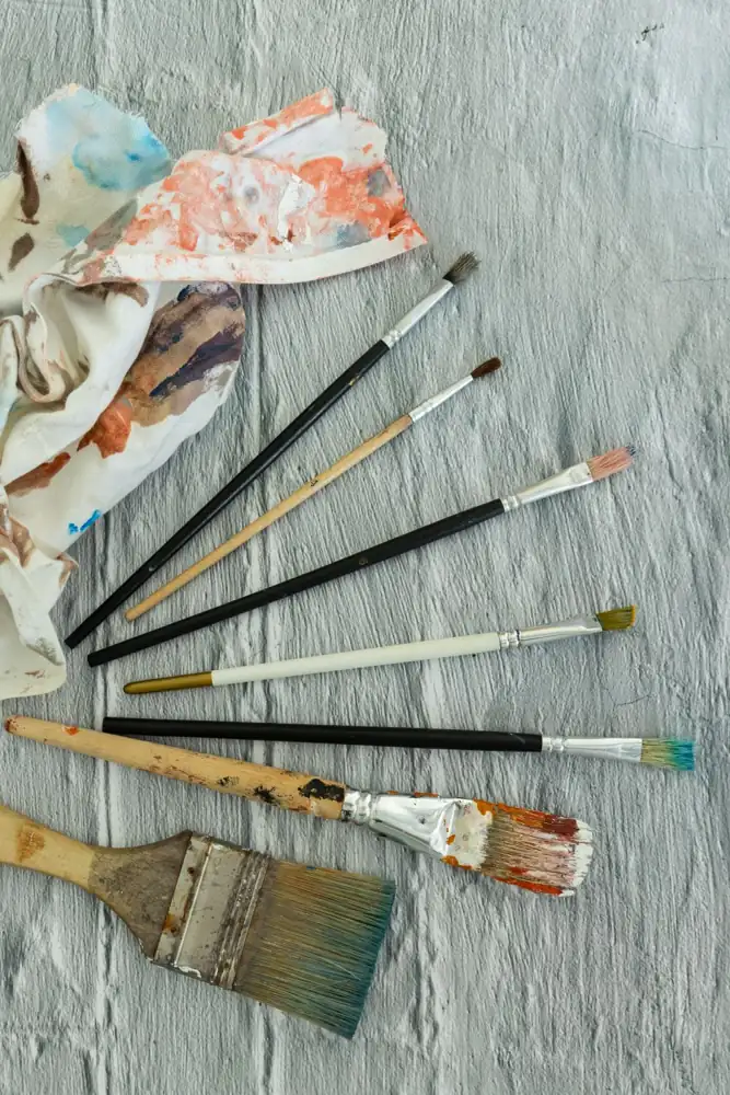 Flat lay of paintbrushes and painted fabric on textured canvas, ideal for art concepts.