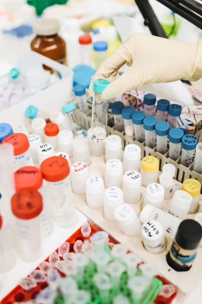 A scientist's gloved hand handling test tubes in a busy laboratory setting.