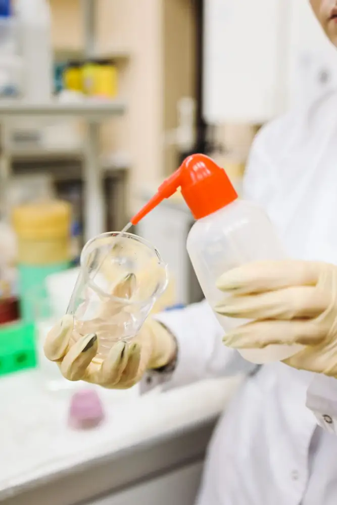 Scientist carefully pouring liquid into a beaker in a laboratory setting, wearing protective gloves.