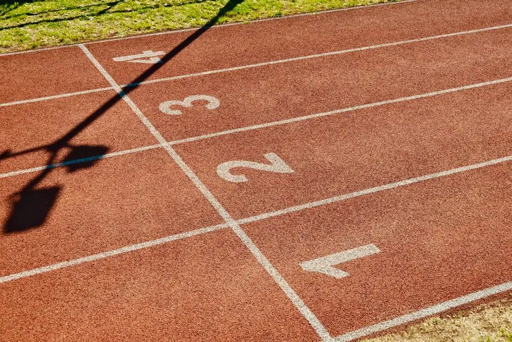 Photograph of a running track with numbered lanes and shadows on a sunny day.