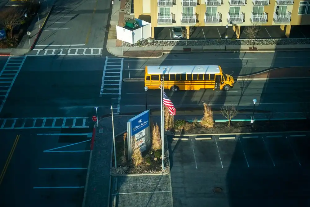 An aerial view of a yellow school bus driving through a quiet city street intersection next to a hotel.