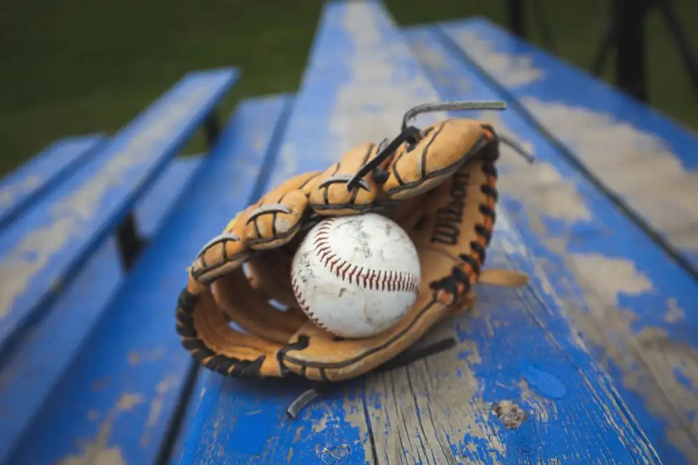 Close-up of a baseball and glove on a blue wooden bench, ready for play.