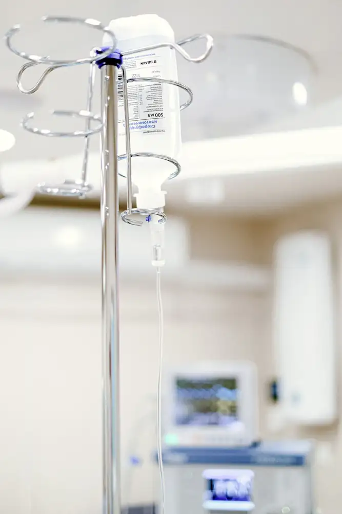 Close-up of an IV drip in a sterile hospital setting with background medical equipment.