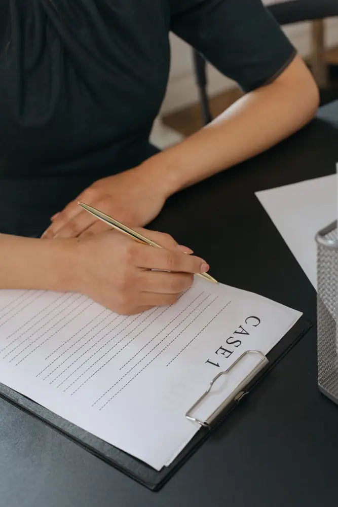Close-up of a woman's hand writing on a case document with a pen in an office environment.