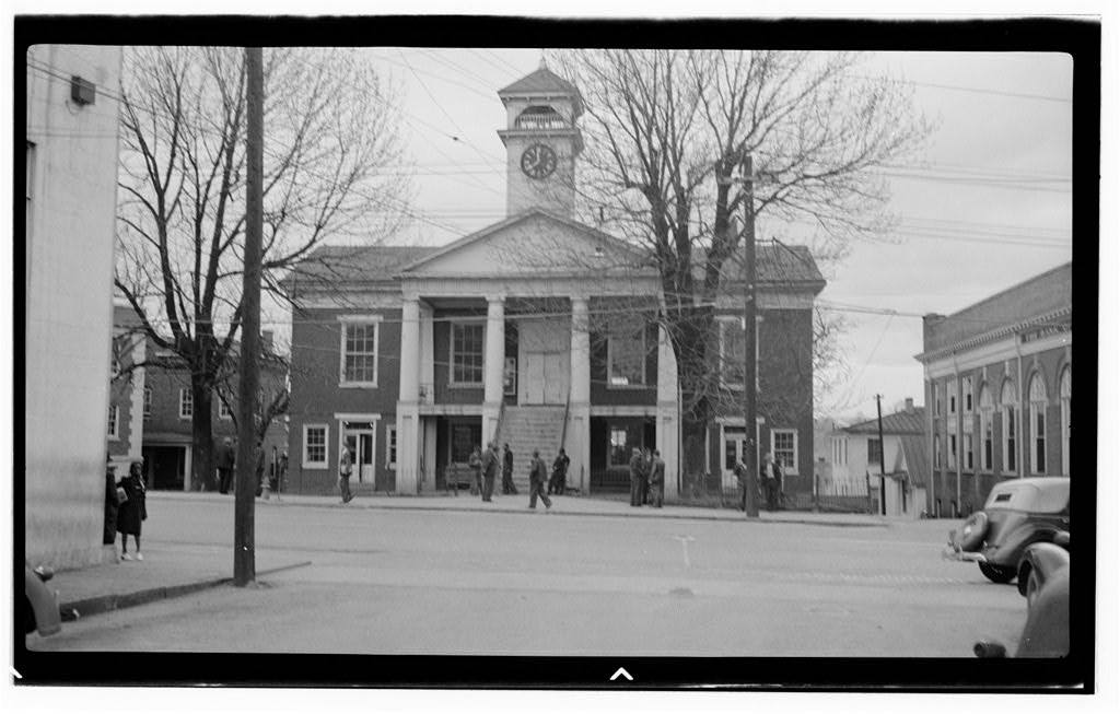 Black-and-white archival photograph of Pittsylvania County Courthouse, with columns, a clock tower, pedestrians and cars.