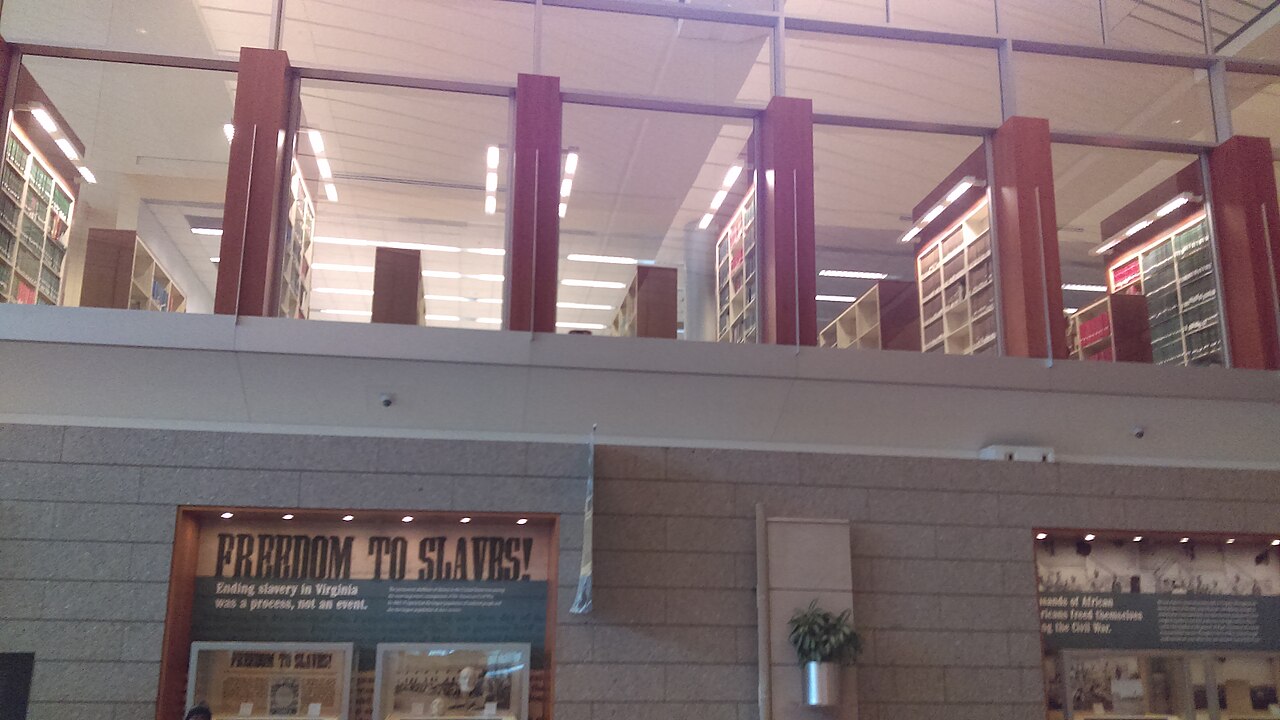 Library of Virginia lobby with an emancipation-history exhibit below glass-fronted upper-floor bookshelves.