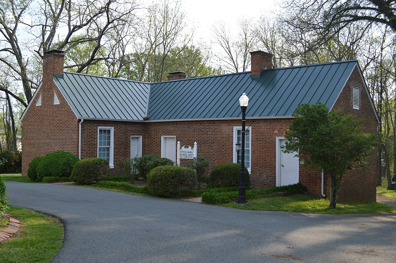 Small historic brick clerk’s office in Chatham with a metal roof, white doors, and a Pittsylvania Historical Society sign.