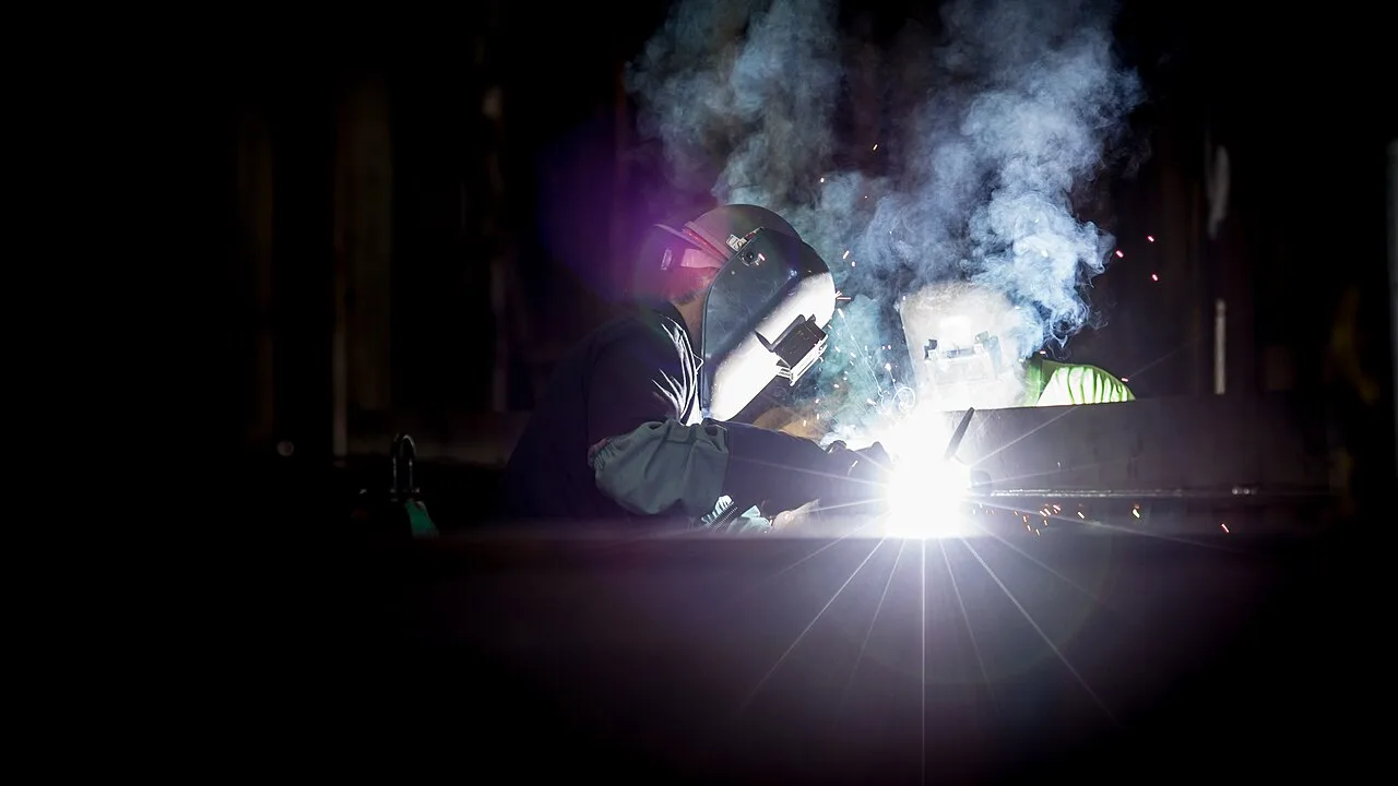 Two workers wearing protective welding helmets amid sparks and smoke